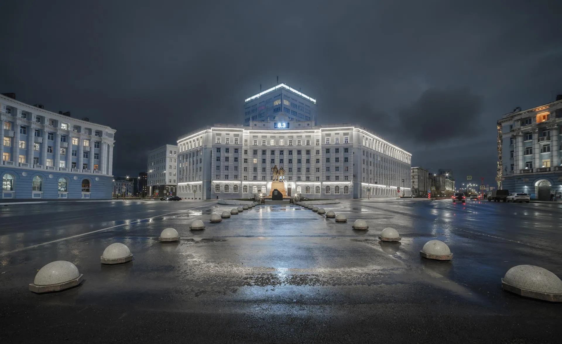 Памятник первопроходцам и здание с подсветкой в центре Норильска.