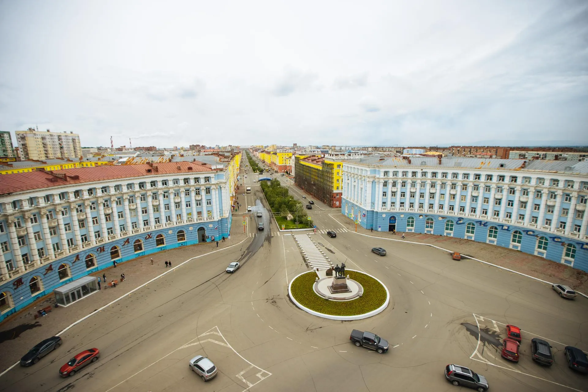 Площадь в центре Норильска с круговым движением и памятником.
